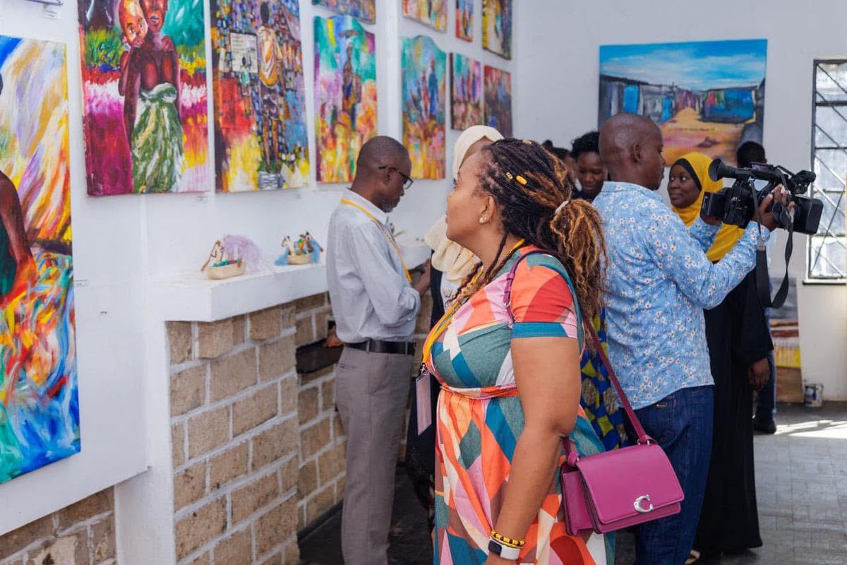 Visitors and a television camera operator moving along a wall of colourful paintings in the gallery.