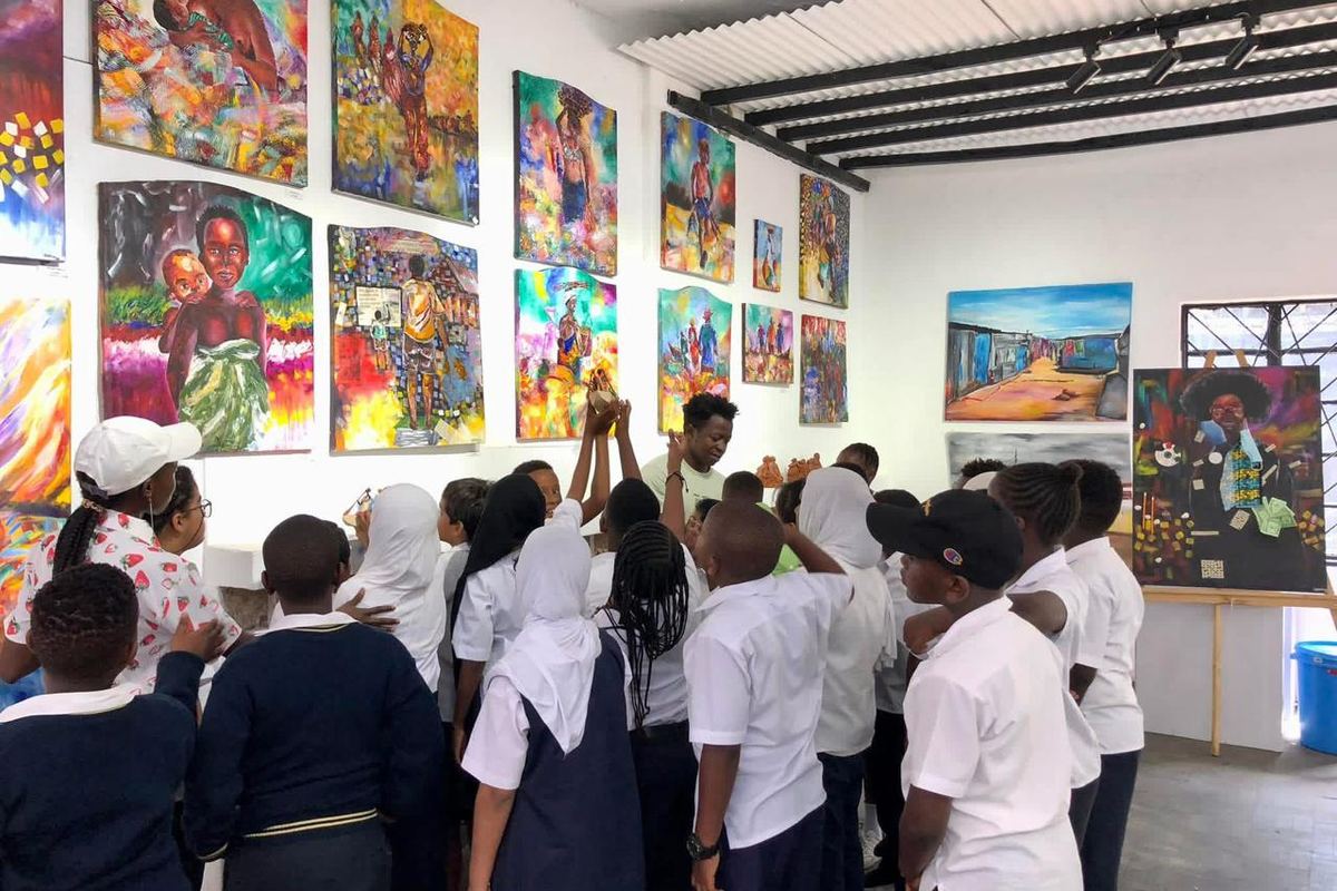 A school group in uniform looking at a wall of brightly coloured paintings with a guide.